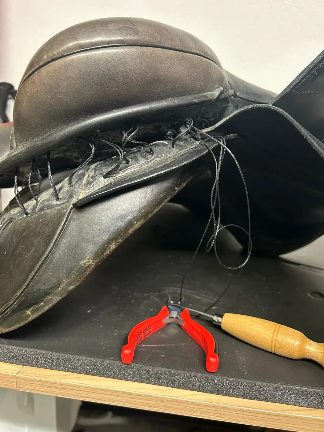 Defekter Sattel mit Zange und Ahle für Reparatur auf Werkbank.